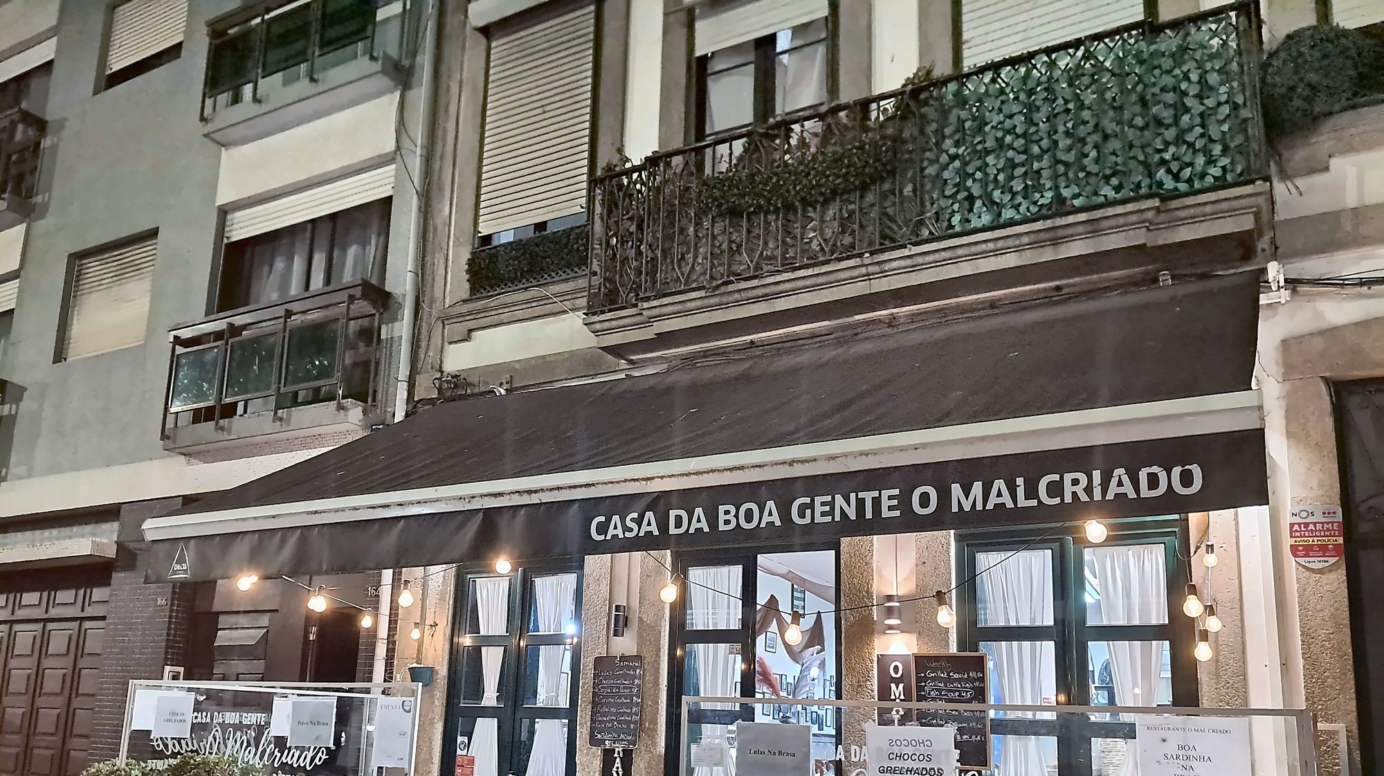 Fachada d'O Malcriado à noite, com o toldo Casa da Boa Gente e luzes de esplanada