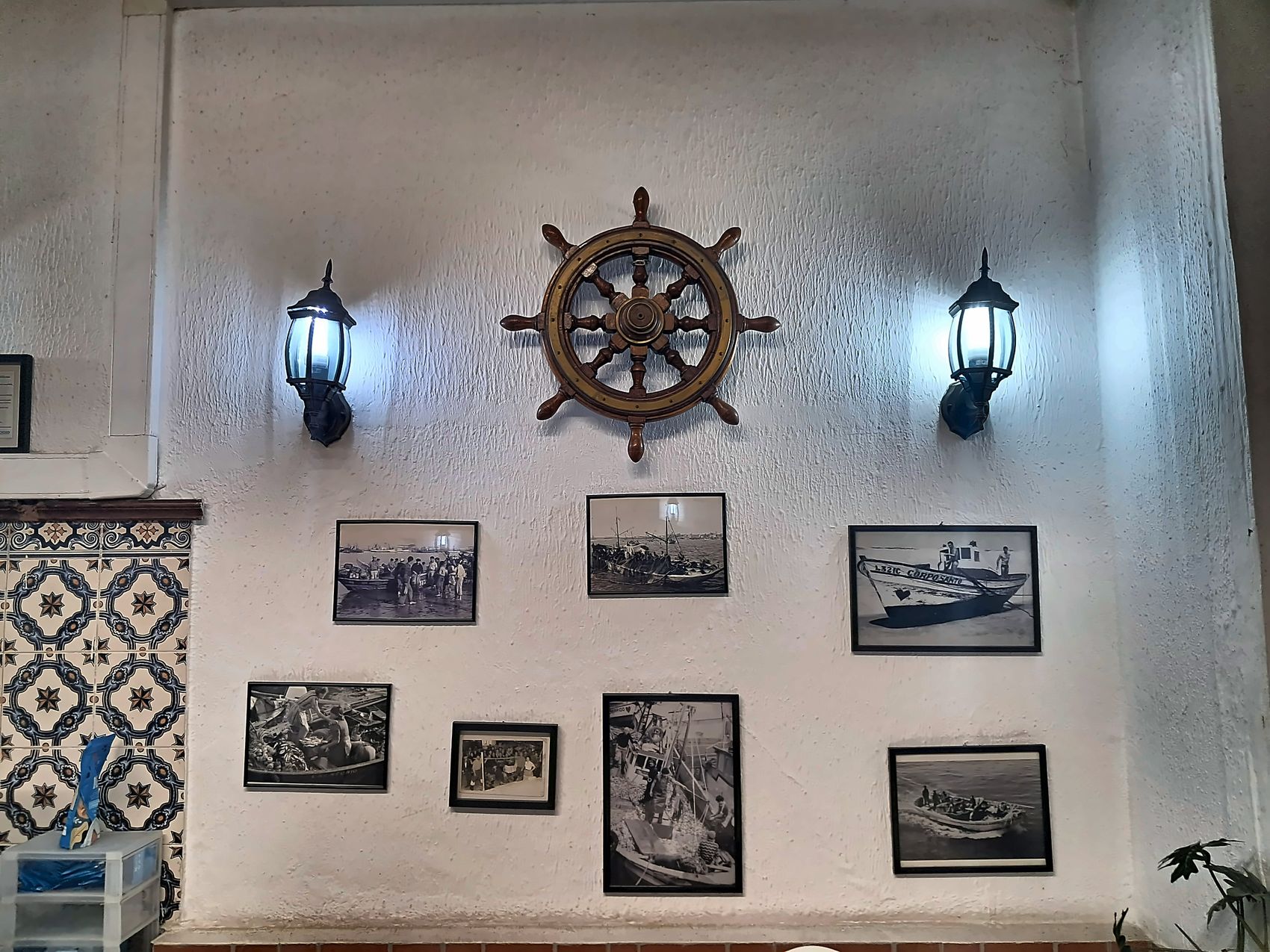 Leme antigo de madeira, candeeiros e fotografias de barcos de pesca
